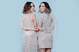 Two twin sisters in shiny evening dresses, holding hands