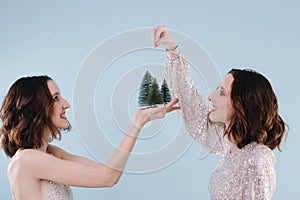 Two twin sisters sprinkle Christmas trees with snow