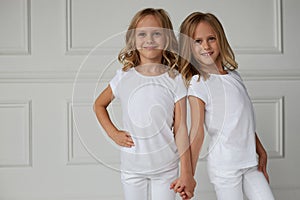 Two twin sisters in white clothes holding hands isolated on a white background. The concept of childhood lifestyle