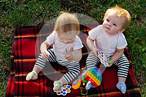 Two twins on a blanket with bright toys look