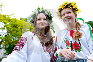 two Ukrainian young women dancing in wind develops hair and flowers near wreath on heads embroidered shirts girls