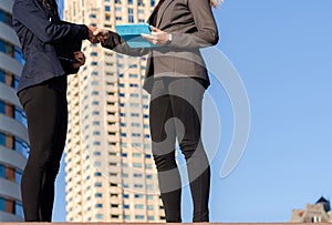 Two unidentifiable young women holding tablets shake hands - business transaction