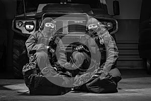 Two uniformed commandos sit in a hangar with a military truck in the background. SWAT concept