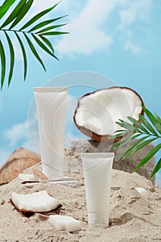 Two unlabeled white cosmetic tubes are placed on the sand, surrounded by fresh coconuts. The scene simulates the sea with white
