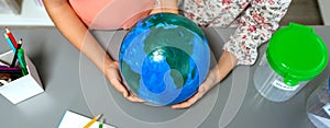 Two unrecognizable female students holding handmade globe world earth