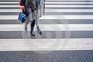 Two unrecognizable persons in black shoes cross wet street after rain on crosswalk, red umbrella, parallel lines