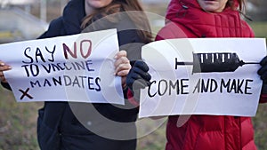 Two unrecognizable women for and against coronavirus vaccination standing with banners arguing. Caucasian activists