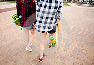 Two urban girls with longboards wearing checkered shirts going along the street in the city