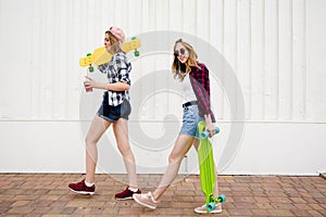 Two urban girls with longboards wearing checkered shirts going along the street in the city