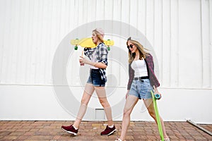 Two urban girls with longboards wearing checkered shirts going along the street in the city