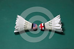 Two used shuttlecocks on green floor of Badminton court with both head each other. One head painted with America flag and one head