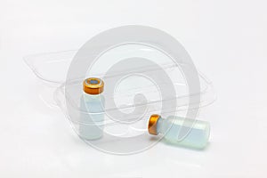 Two vaccine bottle one inside and one outside an opened translucent plastic box for ten vaccine bottles
