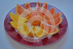 Two varieties of sliced oranges and a whole tangerine in peel on a plate close-up.