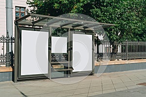 Two vertical blank white billboards at bus stop on city street. In the background buildings and trees. Mock up.