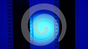Two vertical film strips on a blue background with circular light, close up. 35mm film slide frame. Long, retro film