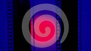 Two vertical film strips on a blue background with pink circular light, close up. 35mm film slide frame. Long, retro