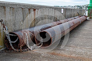Two very large rusty pipes chained to a wall. Construction work and heavy engineering