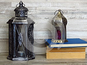 Two very old silver lanterns and a pile of old books on bleached oak background.
