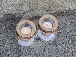 Two vigil candles burn on concrete sidewalk