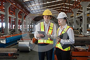 Two vigilant construction workers, amid a bustling factory backdrop, attentively scrutinize a digital tablet, discussing critical photo