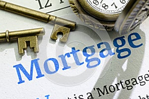 Two vintage brass keys and a pocket watch on a fundamental mortgage instruction manual.