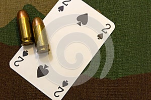 Two vintage pistol bullets and playing card on military camouflage seamless pattern background. Military gambling concept