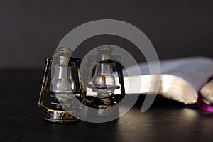 Two vintage rustic ancient lampstands with open Holy Bible Book with golden pages on dark background