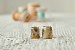 Two vintage thimbles close-up, in the background old wooden bobbins with sewing threads.  Are on the tablecloth antique hand knit