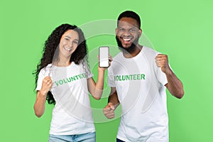 Two Volunteers Showing Phone Screen Gesturing Yes On Green Background