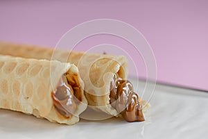 Two waffle cones with sweet boiled condensed milk in white plate on pastel pink background. Condensed tubules.