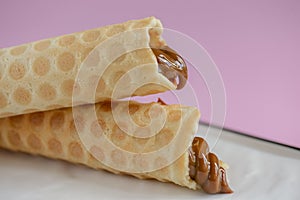 Two waffle cones with sweet boiled condensed milk in white plate on pastel pink background. Condensed tubules.