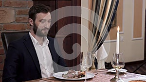 Two waiters simultaneously opens tableware cover - cloche showing the dish in front of the respectable bearded man in a suit. Fine