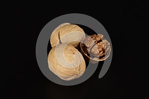 Two walnuts in shell and odi without shell lies next to each other in a black background