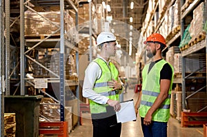 Two warehouse managers in work wear organizing distribution in warehouse storage area.