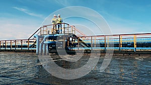 Two wastewater operators observing a sewage cleaning plant from a bridge