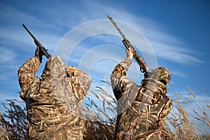 Two waterfowl hunters aiming into sky with guns