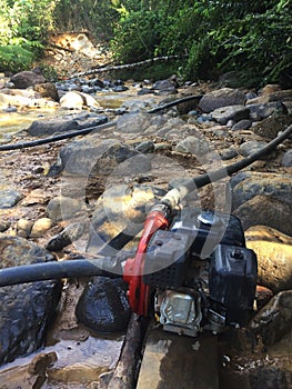 Two waterpumps to pump water for gold mining, the dirt flushes away in the river at the background