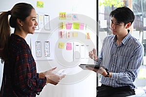 Two website developer presenting and testing mobile app interface design on whiteboard at office.