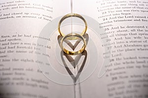 Two wedding Ring on the bible with shadow of heart shape on the page