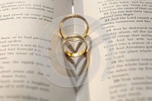 Two wedding Ring on the bible with shadow of heart shape on the page