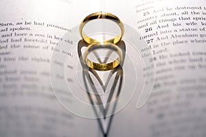 Two wedding Ring on the bible with shadow of heart shape on the page