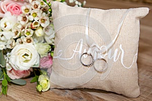 Two wedding rings on brown natural pillow with ribbon and amour love text and flowers bouquet