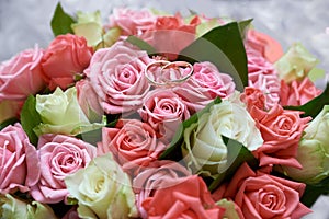 Two wedding rings on colorful bouquet of white, pink and red roses, close up