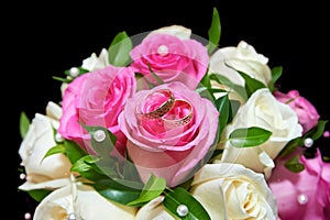 Two wedding rings on colorful bouquet of white and pink roses on black background, close up