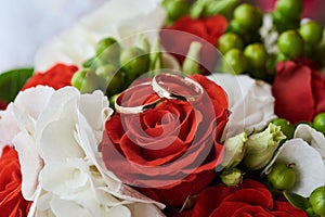 Two wedding rings on colorful bouquet of white and red roses, close up