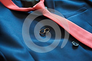 Two wedding rings on groom`s blue suit with red tie