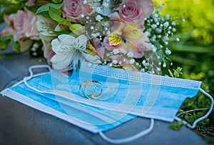 Two wedding rings lie on medical masks on the background of a wedding bouquet. Quarantine Wedding