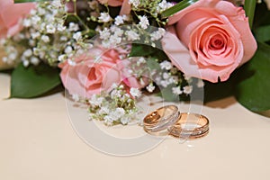 Two wedding rings lie the table.Beckett pink roses.