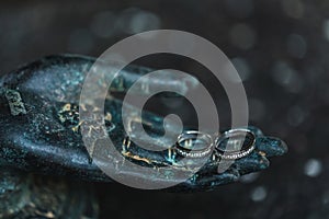 Two wedding rings on metal Buddha hand dark background. Spiritual love concept.