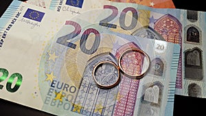 Two wedding rings and money as symbol for an expensive alliance